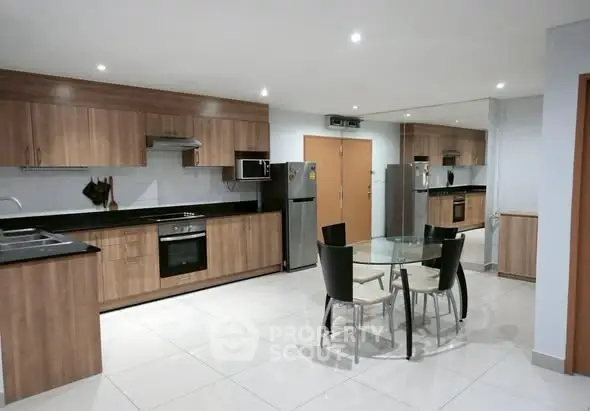 Spacious modern kitchen with wooden cabinets and dining area, featuring sleek appliances and ample lighting.