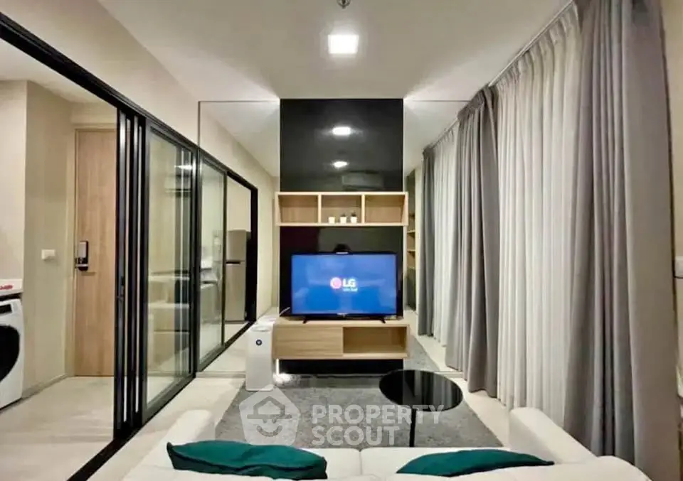 Modern living room with sleek design and glass partitions, featuring a cozy seating area and a flat-screen TV.