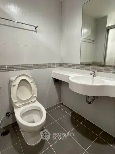 Modern bathroom with sleek fixtures and minimalist design, featuring a wall-mounted sink and tiled flooring.