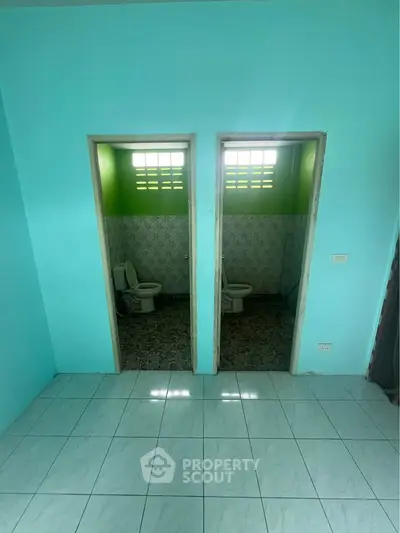 Dual bathroom setup with vibrant teal walls and tiled flooring, offering a unique layout for shared spaces.