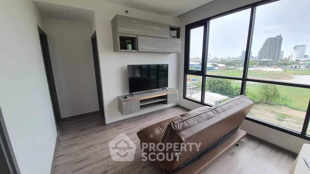 Modern living room with large windows and city view, featuring sleek furniture and wooden flooring.