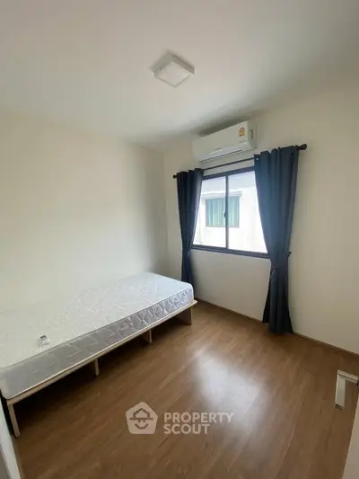 Minimalist bedroom with single bed and air conditioning, featuring wooden flooring and natural light.