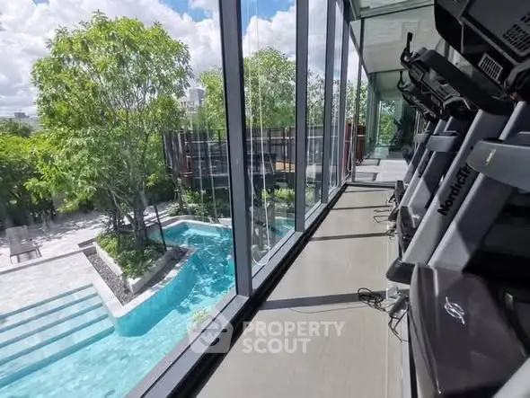 Luxurious gym with panoramic pool view and modern equipment in upscale residential complex.