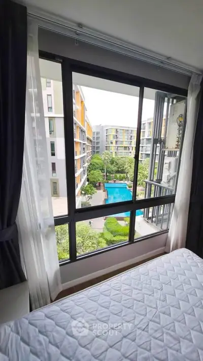 Modern apartment bedroom with large window overlooking pool and garden view.