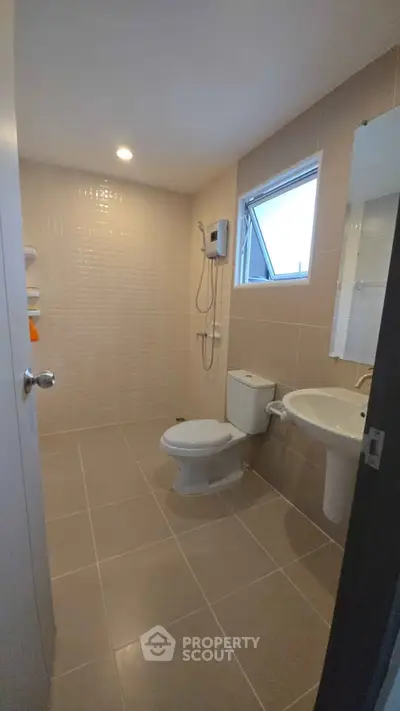 Modern bathroom with sleek fixtures and neutral tiles, featuring a shower and window for natural light.