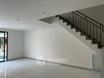 Spacious modern living room with sleek staircase and large windows for natural light.