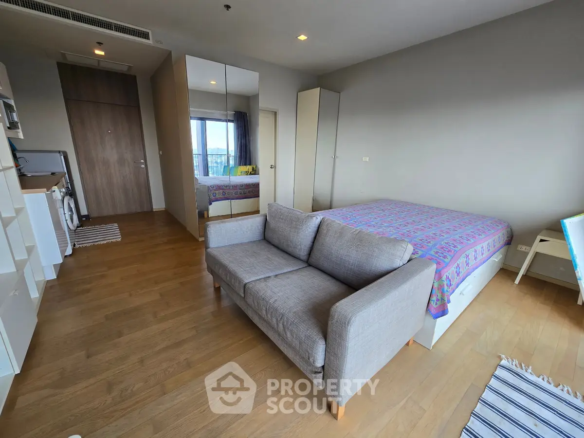 Modern studio apartment with cozy bed, sofa, and mirrored wardrobe on wooden flooring.