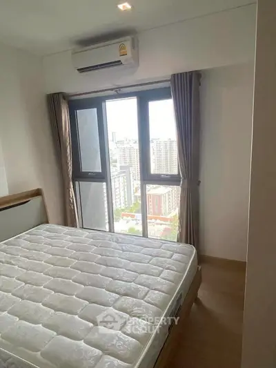 Cozy bedroom with city view, featuring a comfortable bed and large window for natural light.
