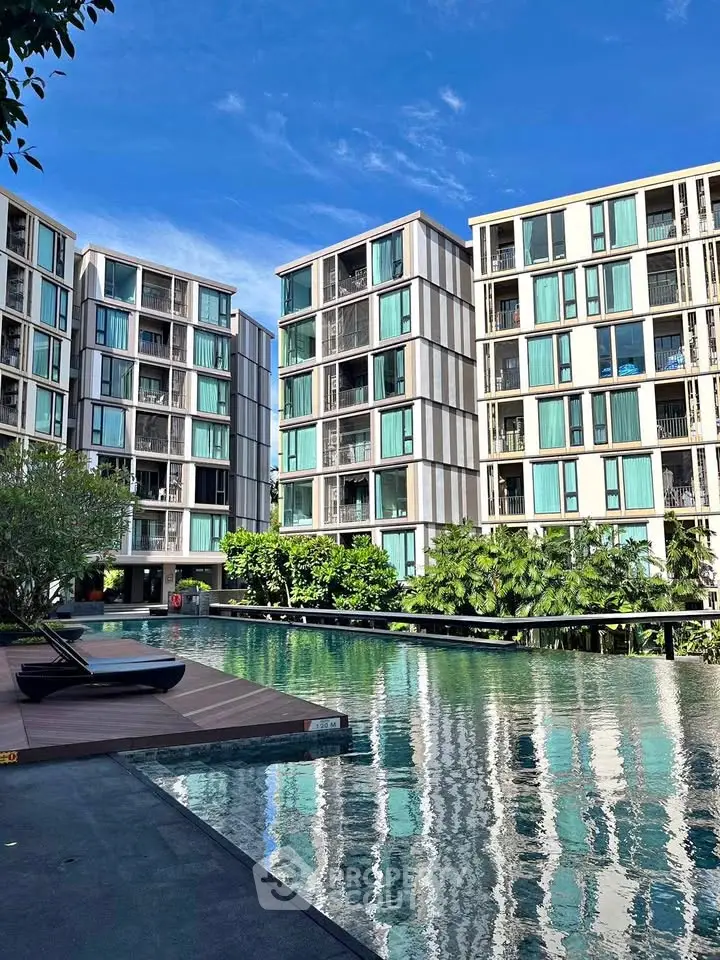 Modern apartment complex with stunning pool and lush greenery under clear blue sky.
