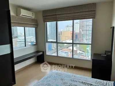 Spacious bedroom with large windows offering stunning city views in a modern high-rise apartment.