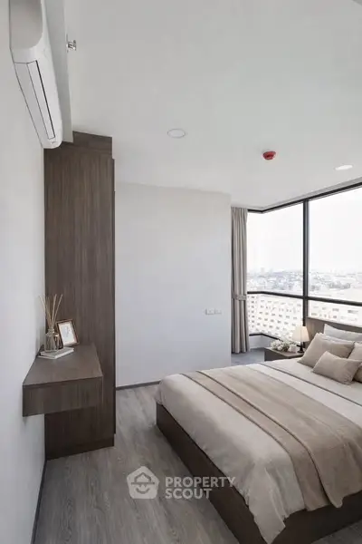 Modern bedroom with large windows offering stunning city views, featuring sleek furniture and neutral decor.