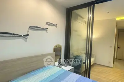 Modern bedroom with sliding glass door to cozy living area, featuring stylish decor and wooden flooring.