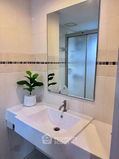 Modern bathroom with sleek sink and mirror, featuring a stylish plant accent.