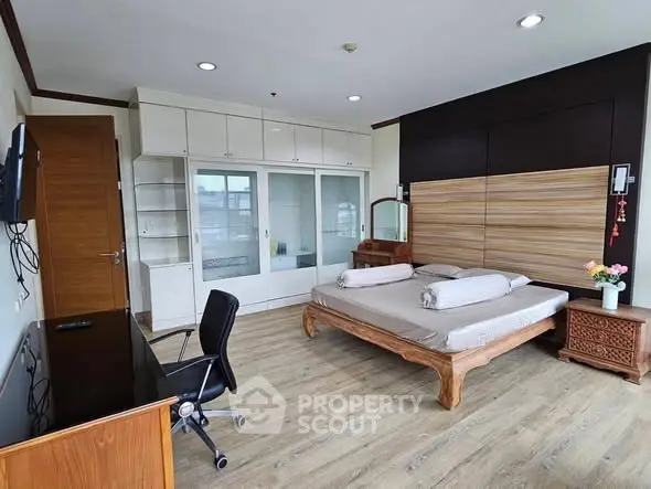 Spacious bedroom with wooden flooring and modern furnishings in a bright apartment.