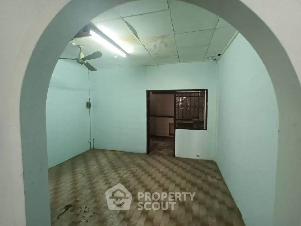 Spacious room with archway and ceiling fan, ideal for renovation.