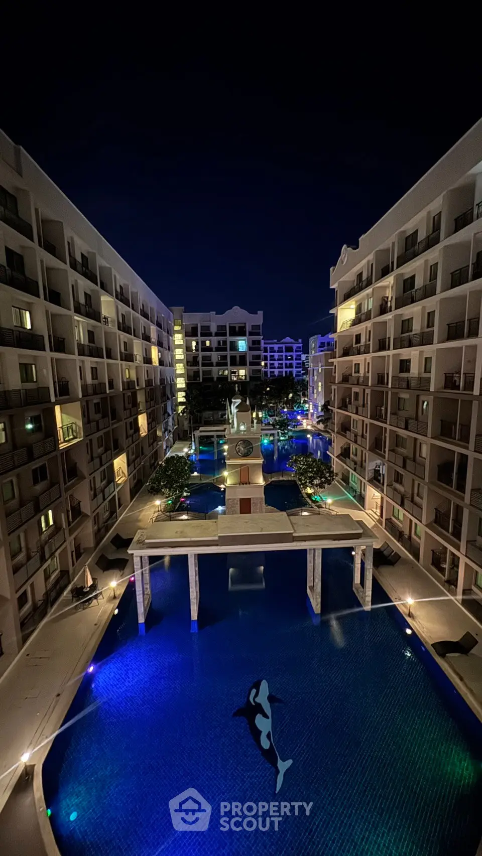Stunning night view of a modern apartment complex with illuminated pool and elegant architecture.