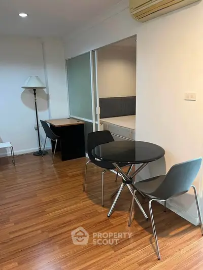 Modern apartment interior with wooden flooring, round dining table, and study area.
