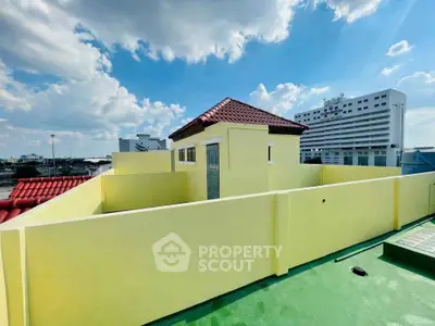 Charming rooftop view with vibrant yellow walls and cityscape backdrop under a clear blue sky.