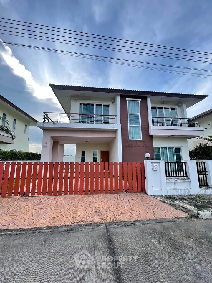 Modern two-story house with balcony and red fence in a suburban neighborhood.