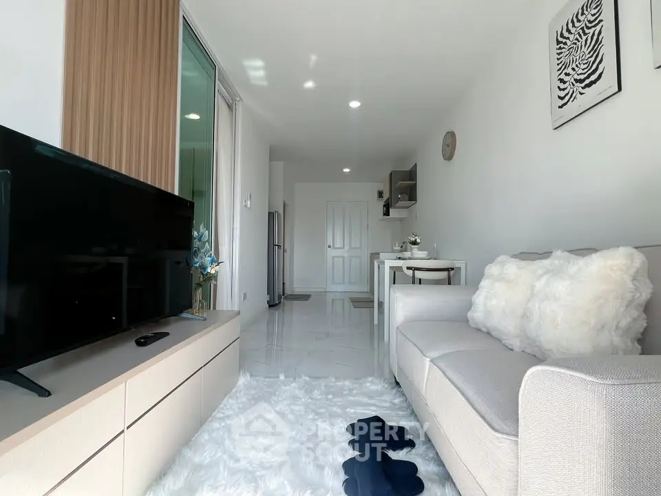 Modern living room with cozy decor, plush rug, and sleek TV setup in a bright apartment.