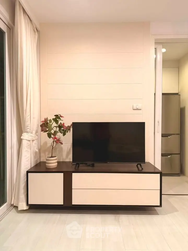 Modern living room with sleek TV stand and elegant decor, adjacent to a bright kitchen area.