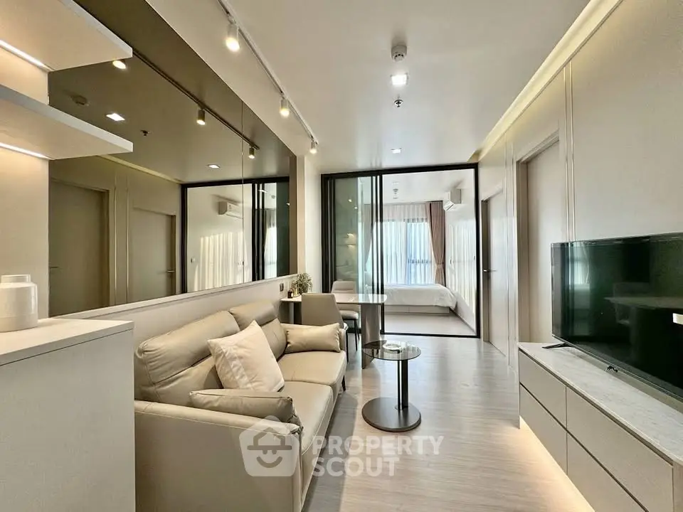 Modern living room with sleek design and glass partition leading to bedroom, featuring neutral tones and stylish decor.