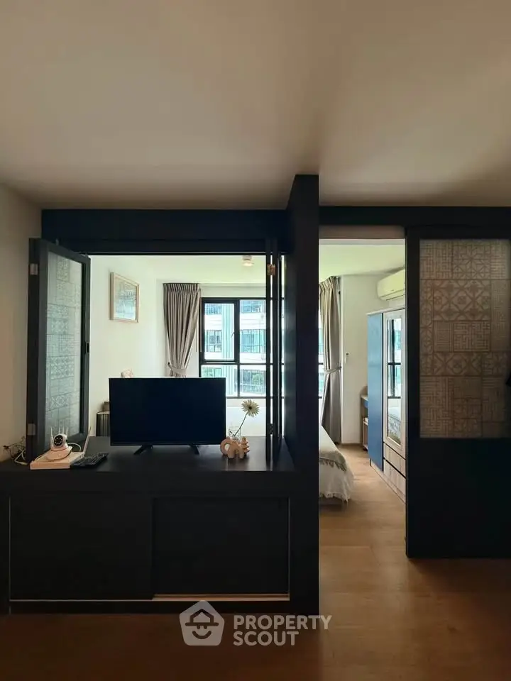 Modern living room with TV and sliding doors leading to a cozy bedroom, featuring elegant decor and natural light.