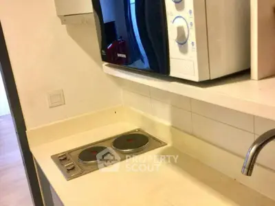 Compact kitchen with electric stove and microwave in modern apartment.