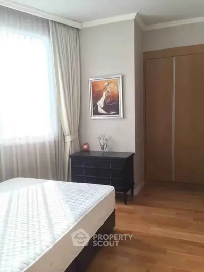 Spacious bedroom with wooden flooring and elegant decor in modern apartment.