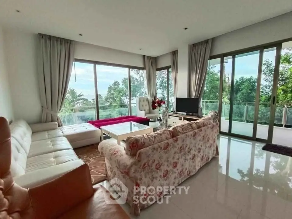 Spacious living room with large windows and lush garden view, featuring elegant sofas and modern decor.