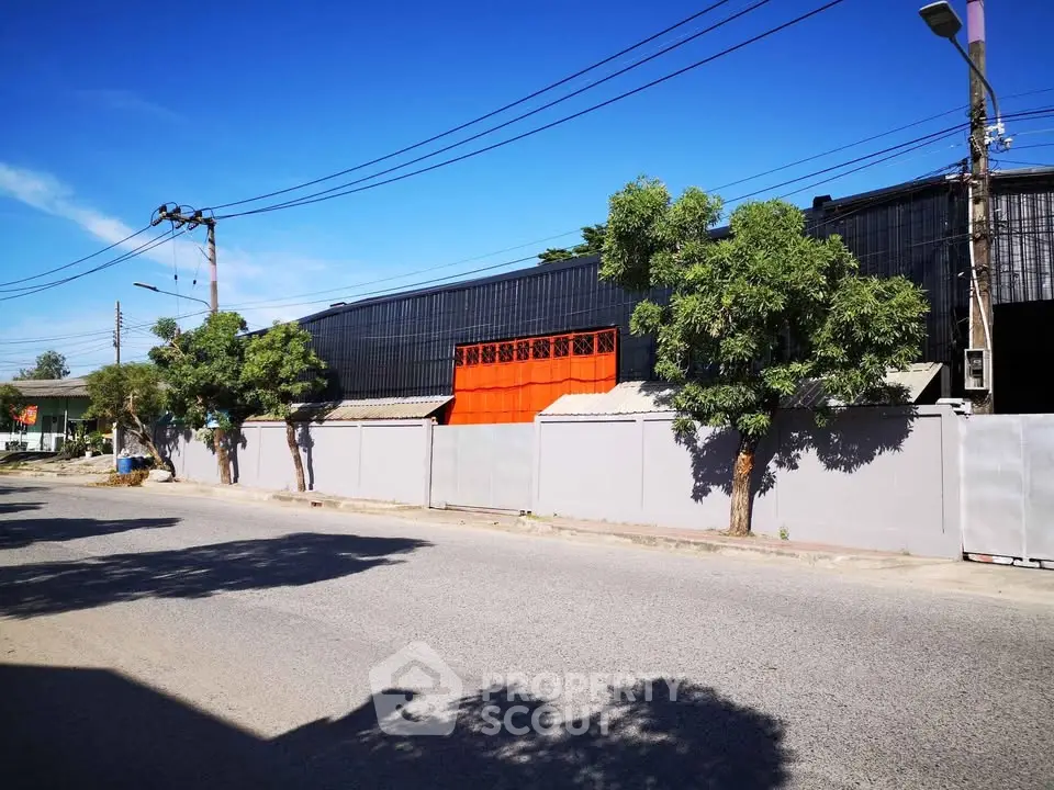 Industrial building exterior with vibrant orange gate and surrounding trees.