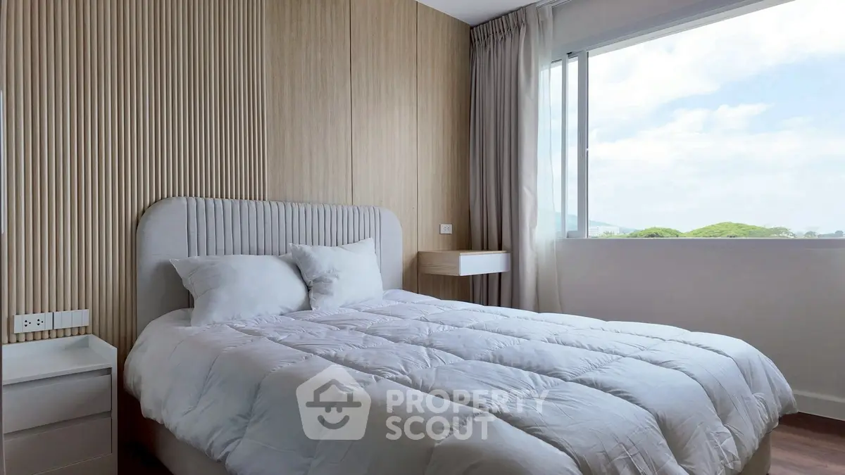 Cozy bedroom with modern decor and large window offering natural light and scenic view.