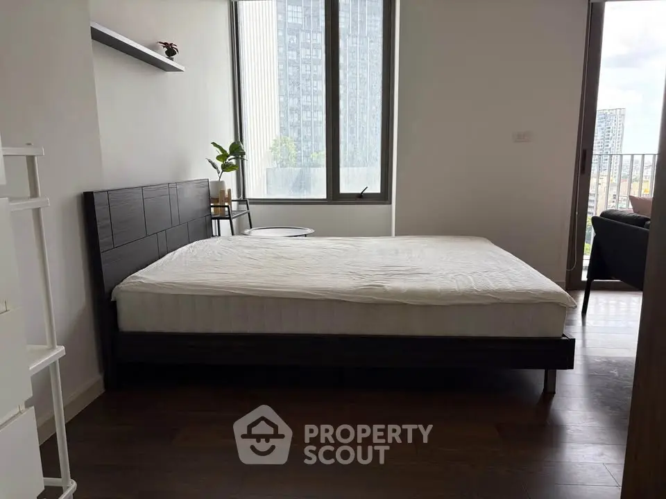 Modern bedroom with large windows and city view, featuring a sleek bed and minimalist decor.