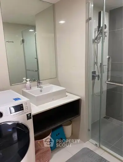 Modern bathroom with glass shower and washing machine in sleek apartment.