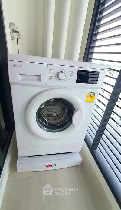 Modern washing machine in a bright laundry area with large windows.