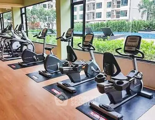 Modern gym with exercise bikes and pool view in luxury apartment complex.
