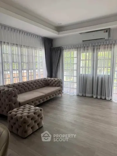Spacious living room with elegant tufted sofa and large windows offering natural light.