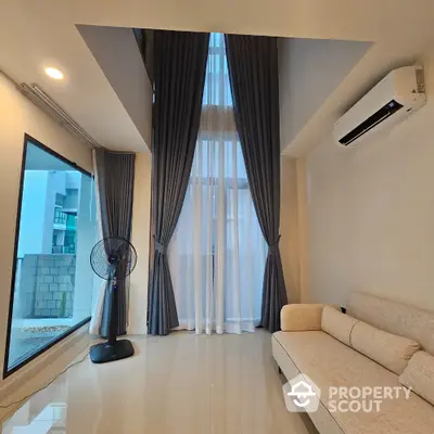 Modern living room with high ceilings, large windows, and elegant curtains in a stylish apartment.