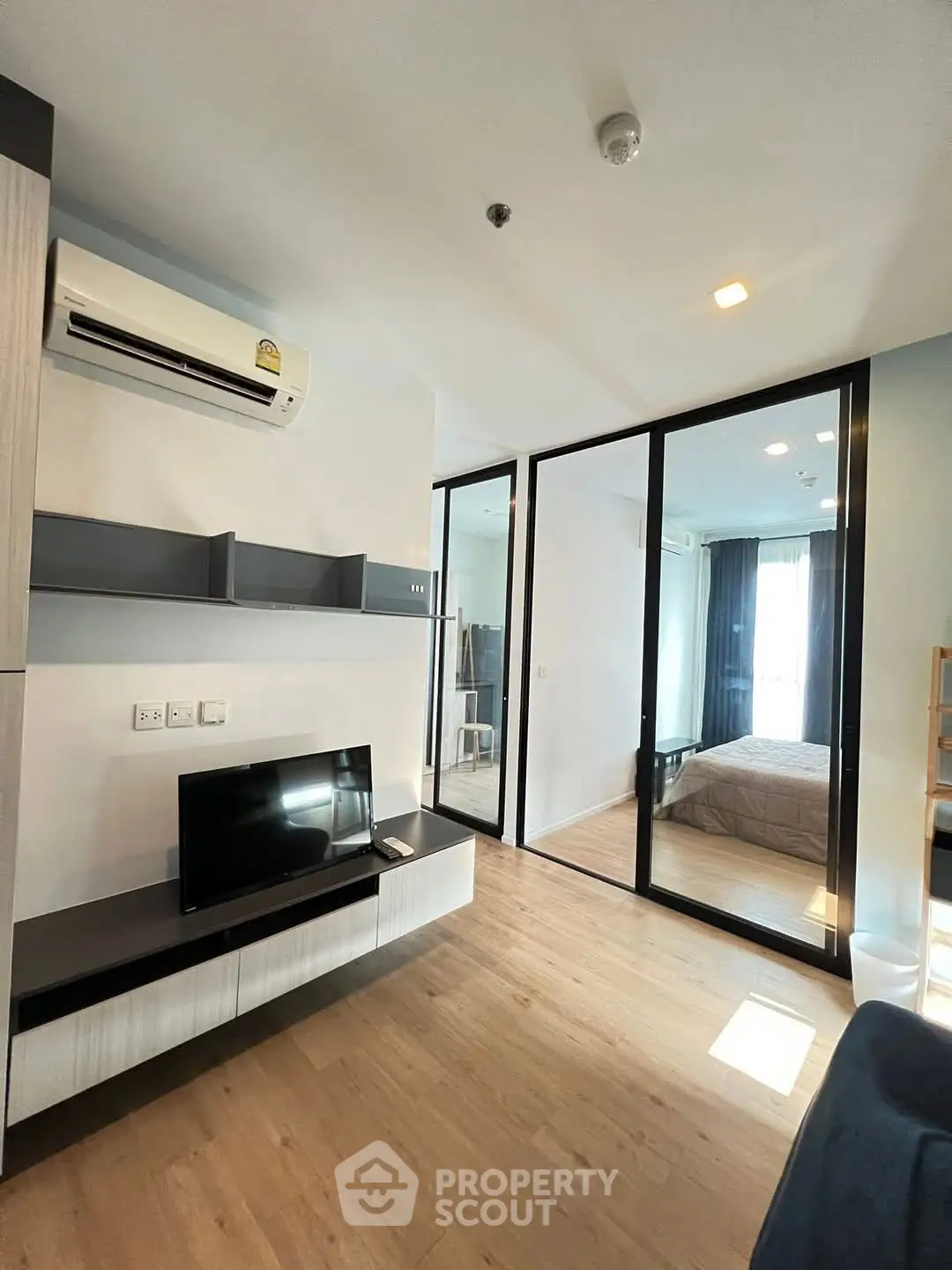 Modern living room with sleek design and glass partition leading to cozy bedroom.