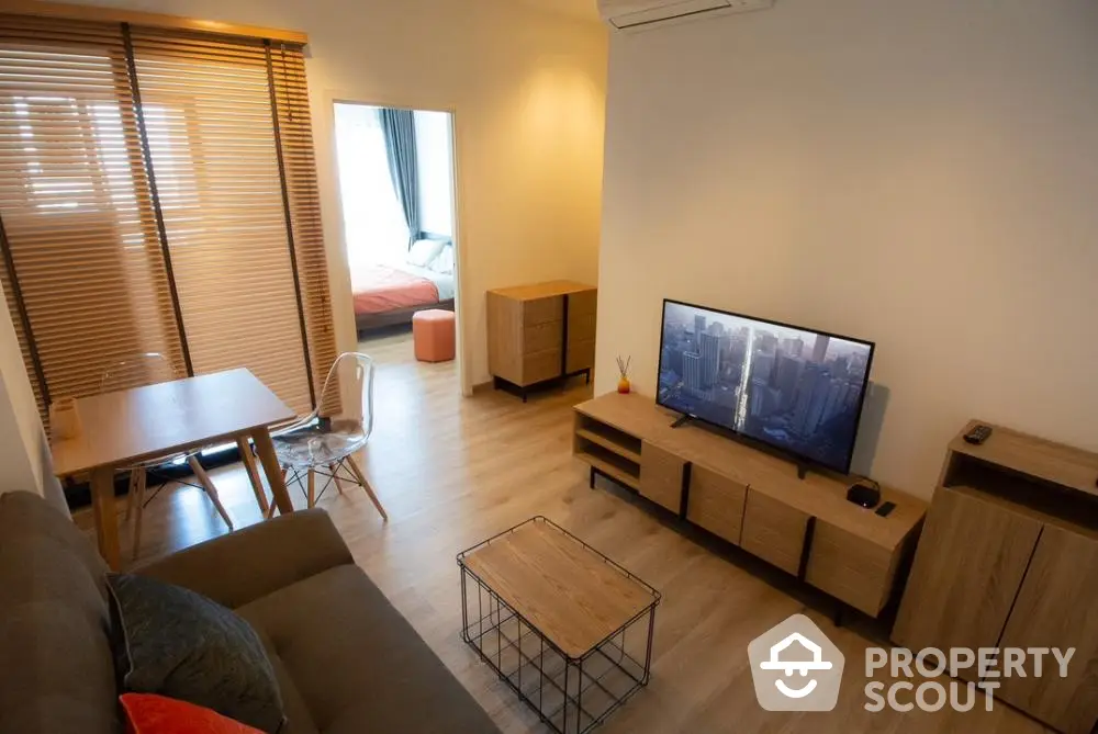 Spacious modern living room with ample natural light, featuring a cozy sofa set, flat-screen TV, and a dining area that seamlessly connects to a comfortable bedroom space.