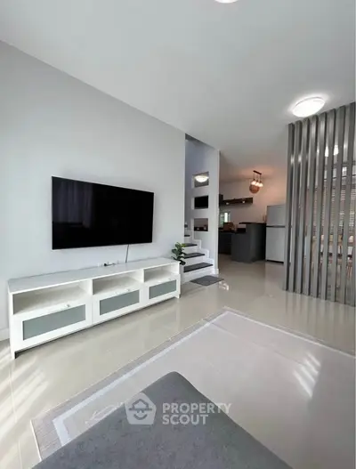 Modern living room with sleek TV setup and open kitchen layout in stylish apartment.