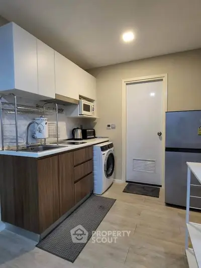 Modern kitchen with sleek cabinets, washing machine, and compact fridge in a cozy apartment.