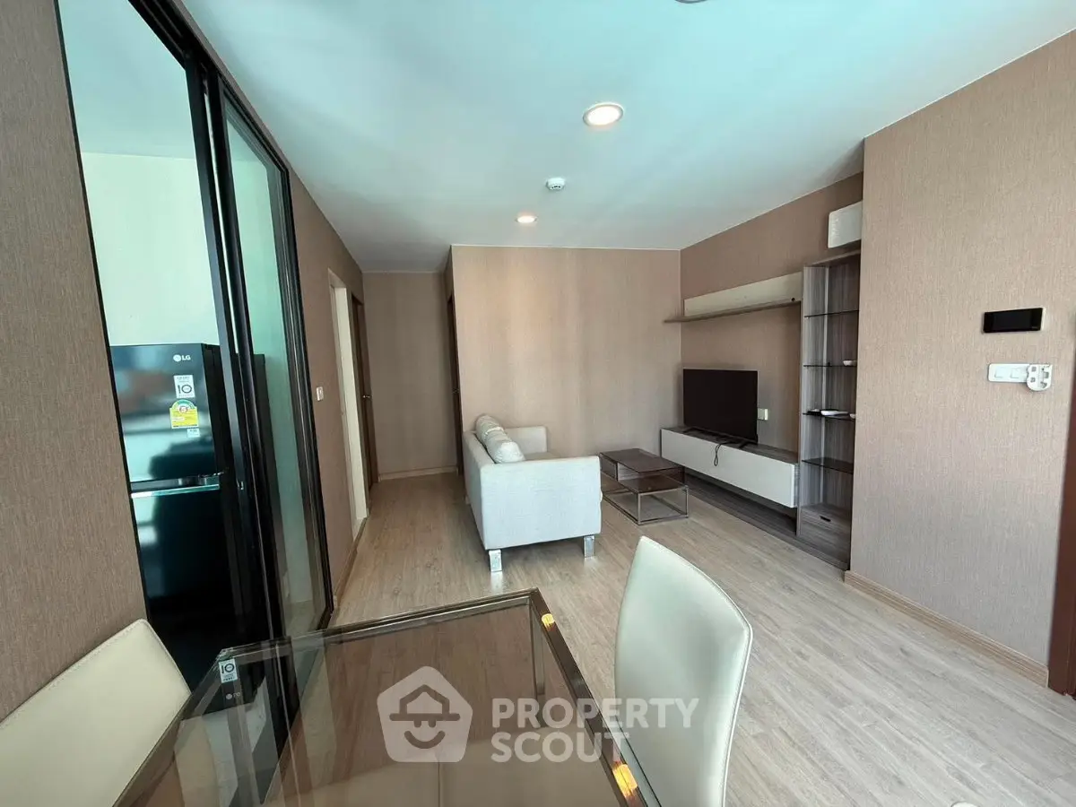 Modern living room with sleek furniture and open layout, featuring a glass dining table and wall-mounted TV.