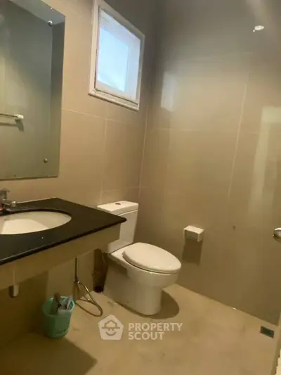 Modern bathroom with sleek fixtures and neutral tones, featuring a large mirror and window for natural light.