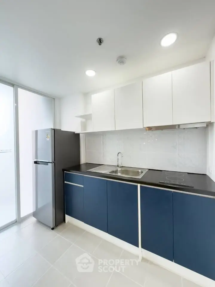 Modern kitchen with sleek blue cabinets and stainless steel appliances in a bright apartment.