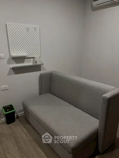 Modern minimalist living room with sleek gray sofa and wall-mounted pegboard for storage.