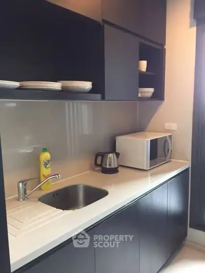 Modern kitchen with sleek cabinetry and appliances, featuring a microwave and kettle.