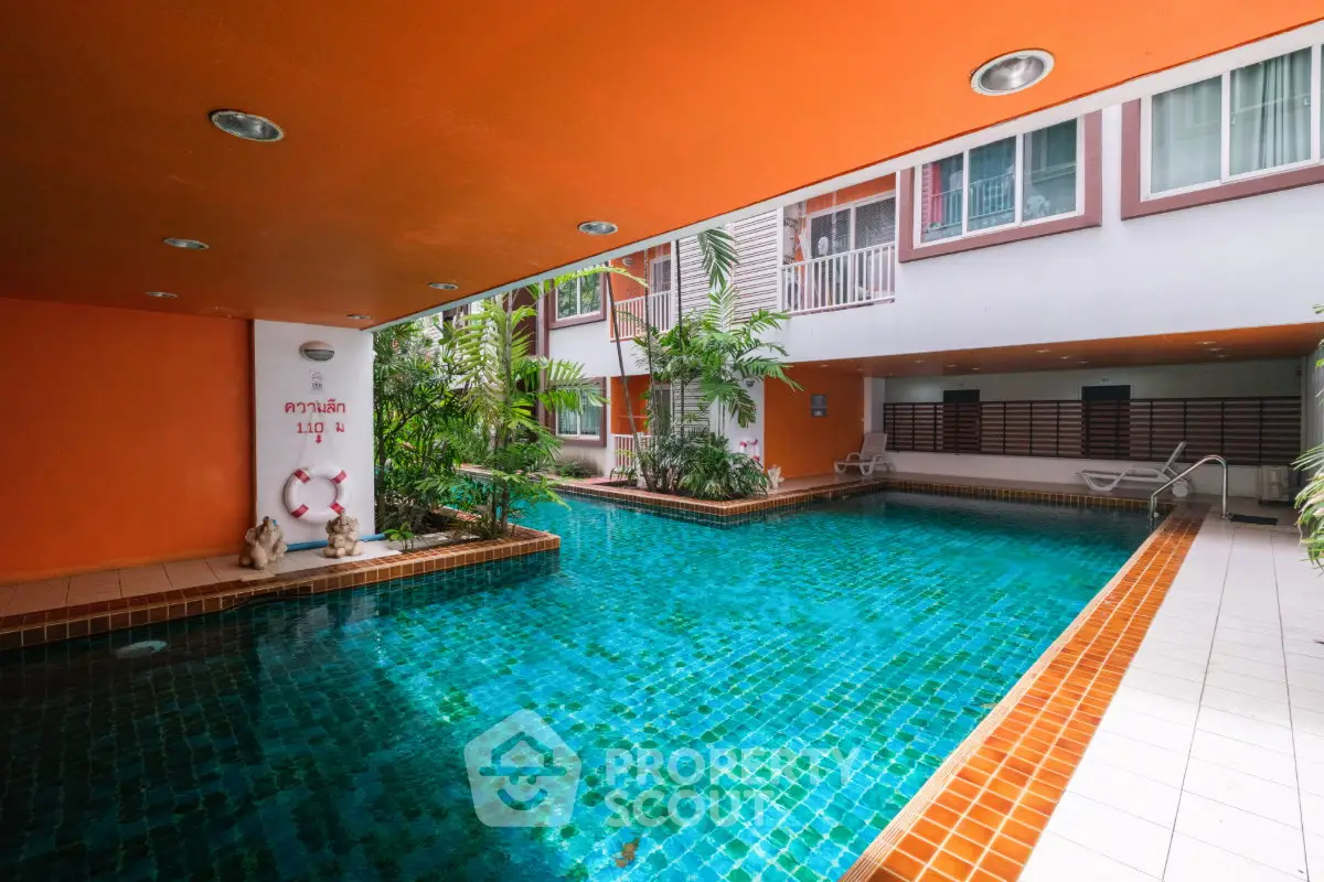 Stunning indoor pool area with vibrant orange accents and lush greenery in a modern residential complex.