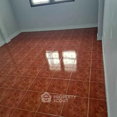 Spacious empty room with glossy red tile flooring and large window.