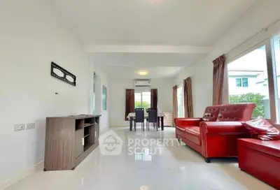 Spacious living room with modern red leather sofas and dining area, featuring large windows for natural light.